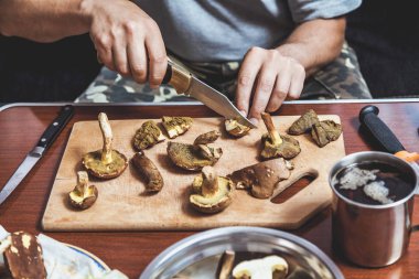 Toplanan mantarların incelenmesi. Tahta bir yaban domuzunun üstünde yenebilir mantar kesen bir adamın elleri.