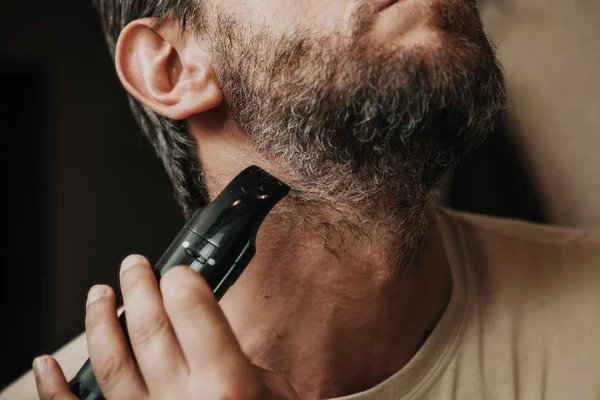 beard trimmer trimmer. The man independently cuts his gray beard with a machin