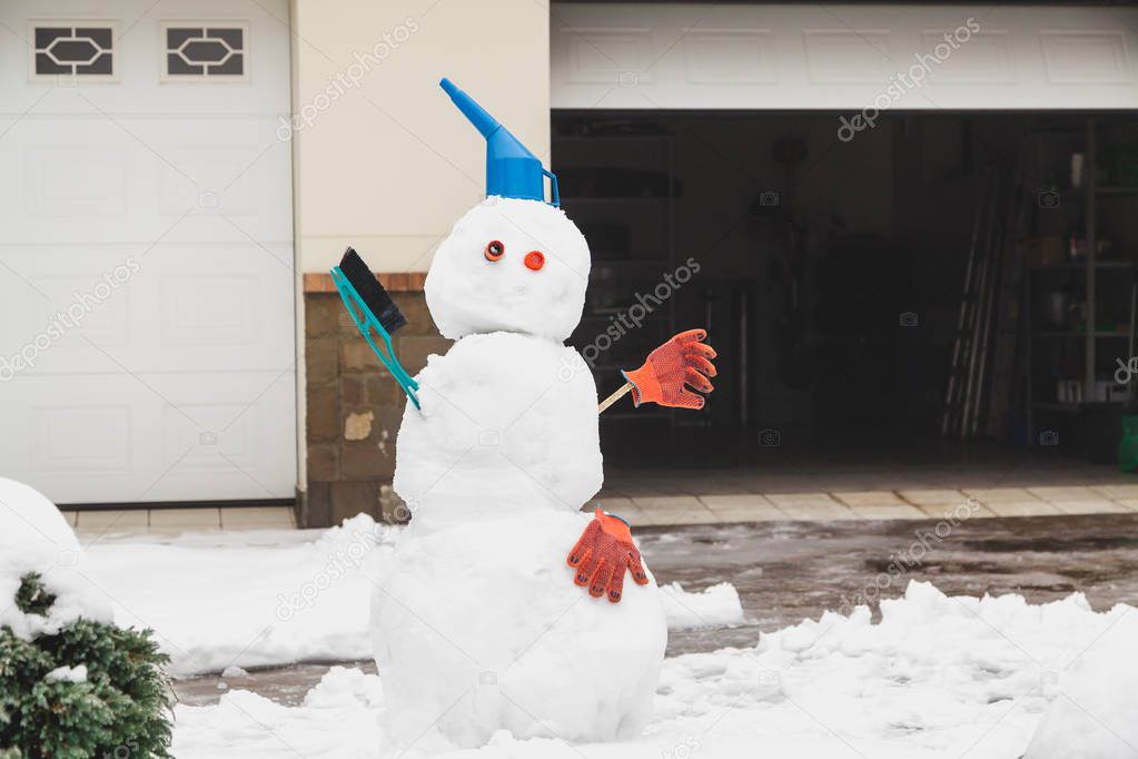 Snowman motorist stands in front of the garage. For decoration use a watering can, a brush and working glove