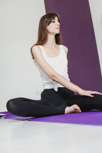 Cute graceful girl with long hair in tights engaged in yoga on a lilac ru