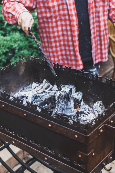 在烤架上准备煤 一个穿红格子衬衫的男人在锻造的 Brazie 中采摘热煤 — 图库照片