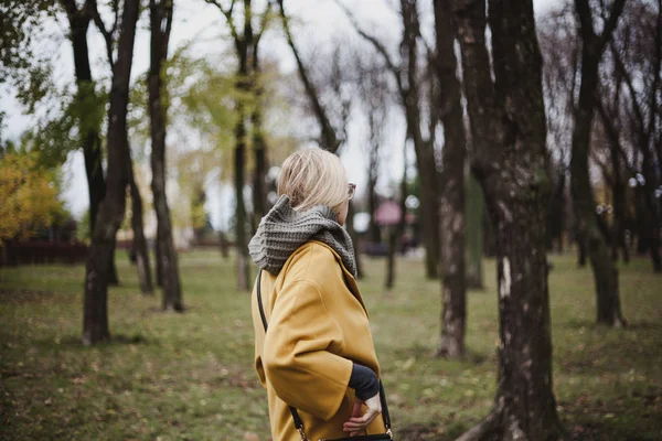 在秋天的公园里 穿着鲜艳的黄色时装大衣的纤细的金发女郎走了 Bac — 图库照片