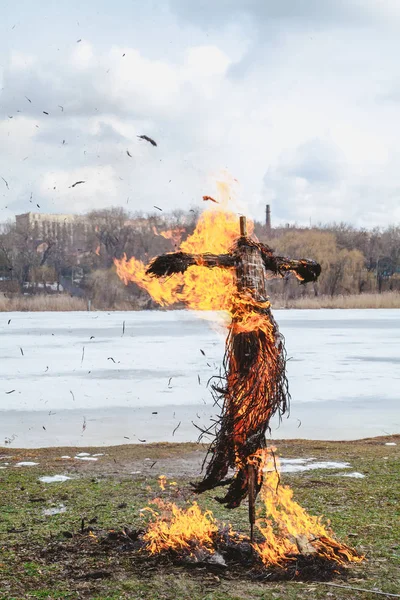 Slavic holiday of the end of winter. A large Shrovetide doll from straw burns on the river bank. Black smoke is visible