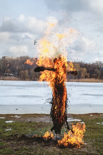 Slavic holiday of the end of winter. A large Shrovetide doll from straw burns on the river bank. Black smoke is visible