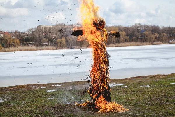 Slavic holiday of the end of winter. A large Shrovetide doll from straw burns on the river bank. Black smoke is visible