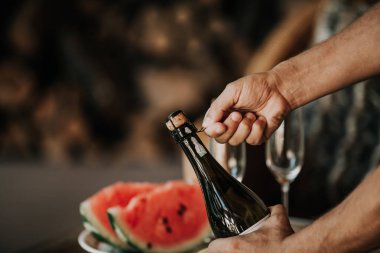 Elinde bir şişe köpüklü şarap muse twist. Cam masaya bir tabak karpuz ve frui ile geri