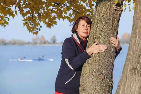 Roztomilý Starší Žena Objímala Kmen Stromu Břehu Rybníka Podzimní Slunečný — Stock fotografie