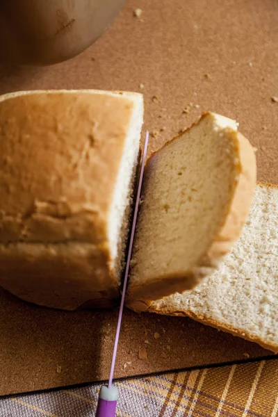 Slicing a loaf of bread. A large knife cuts thin pieces of white bread from a rectangular loaf. View from abov