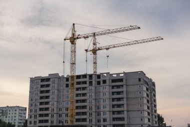 İnşaat site mükemmeliyetçiliği. Uzun bir çok katlı ev bir bulutlu gökyüzü adam karşı iki sarı vinçler inşa