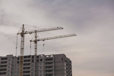 İnşaat site mükemmeliyetçiliği. Uzun bir çok katlı ev bir bulutlu gökyüzü adam karşı iki sarı vinçler inşa