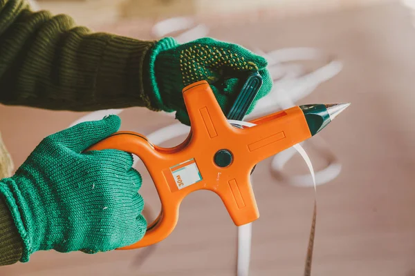 Hands in green gloves wind a steel band on an orange geodetic roulett