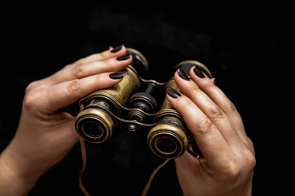Binoculars and a woman. Beautiful female hands with manicure hold vintage metal binocular