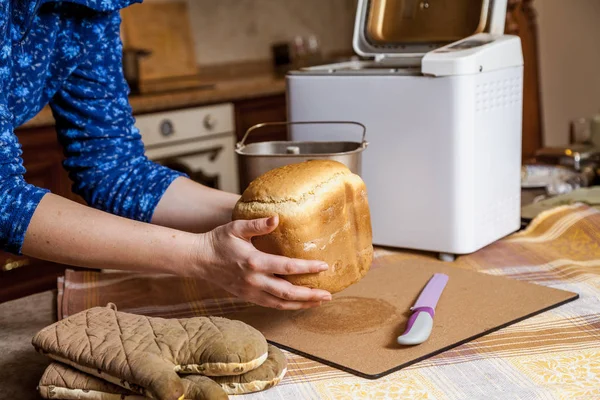 女人手从电动面包机的面包烘焙模具中拿出新鲜的面包 附近有一把大刀子 — 图库照片