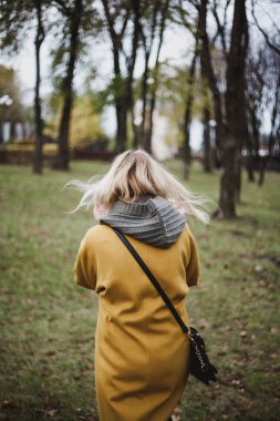 parlak sarı moda ceket ince sarışın sonbahar bir parkta yürüyor. Bac görüntülemek