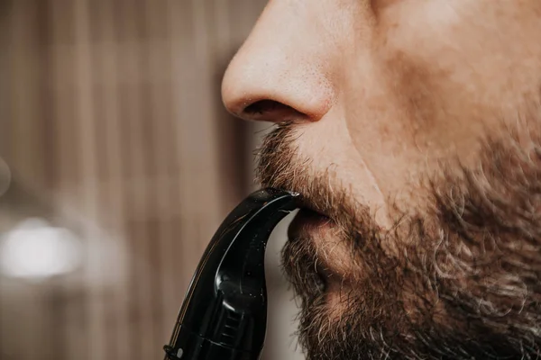 Haircut beard trimmer. A man cuts his mustache with a machin