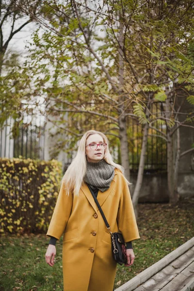 一个年轻女子的肖像在一个黄色的大衣在一个秋季标准的长金发的眼镜 — 图库照片