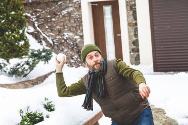 Hava kar oyunları. Bir sıcak yelek ve şapka bir sakallı bir adam bir soğuk da özel evde avlusunda kartopu atar