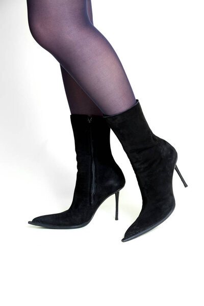 Slender female legs in fashionable black suede boots with narrow socks and high thin heel on a white background. Side vie