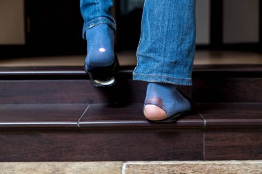 Holes in fashion. Legs in denim pants with big holes on blue socks go up the stairs in the roo clipart