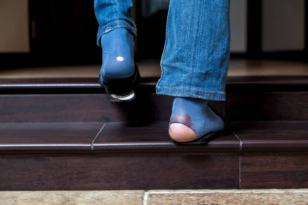 Holes in fashion. Legs in denim pants with big holes on blue socks go up the stairs in the roo