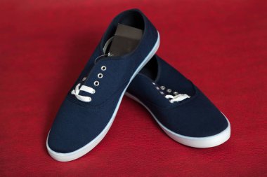 Beyaz tabanlı ve bağcıklı iki yeni mavi spor ayakkabı kırmızı izole bir arka planda duruyor.