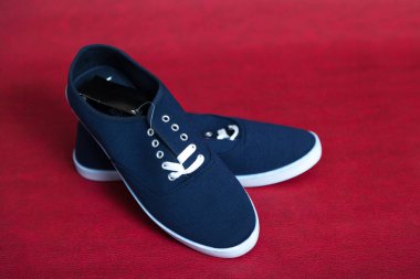 Beyaz tabanlı ve bağcıklı iki yeni mavi spor ayakkabı kırmızı izole bir arka planda duruyor.