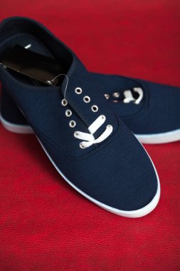 Beyaz tabanlı ve bağcıklı iki yeni mavi spor ayakkabı kırmızı izole bir arka planda duruyor.