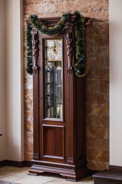 Saat yüksek kat bir kahverengi ahşap oyma durumda bir yılbaşı garlan ile dekore edilmiştir.