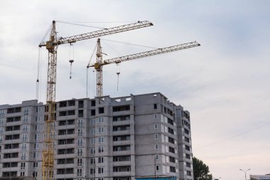 İnşaat site mükemmeliyetçiliği. Uzun bir çok katlı ev bir bulutlu gökyüzü adam karşı iki sarı vinçler inşa