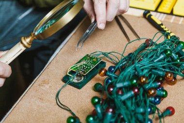 Yeni yıl için hazırlanıyor. Köknar ağacı elektrik çelenk tamiri. Birinde bir büyüteç ver. Sağ el cımbız