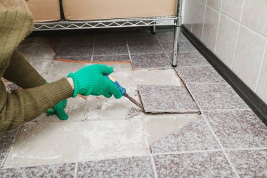 Fayansların sökülmesi. Yeşil eldivenli eller, kırık fayansı keskiyle baltalıyor.