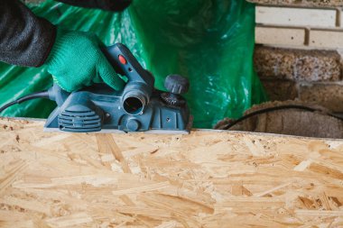 Yeşil çalışma eldiven elinde elektrikli bir planı ile ahşap plaka kenarını işlemek
