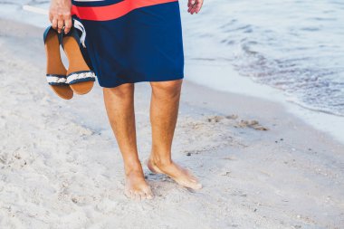 Kadın onun elinde sandal ile kumlu bir plaj boyunca yürür