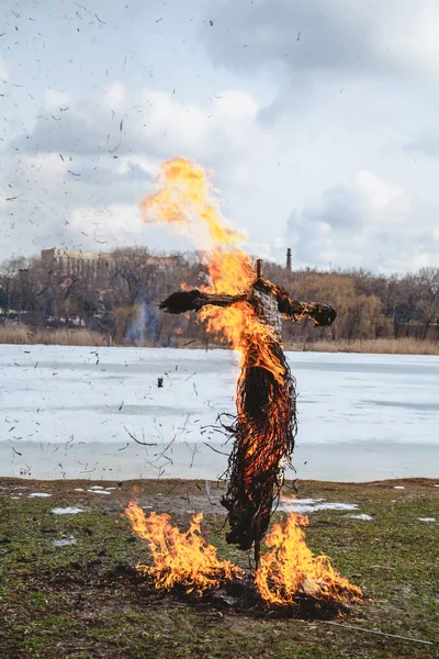 Slavic holiday of the end of winter. A large Shrovetide doll from straw burns on the river bank. Black smoke is visible