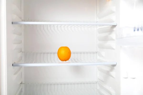 Orange in the fridge. A beautiful orange lies on the second shelf of an empty modern refrigerato