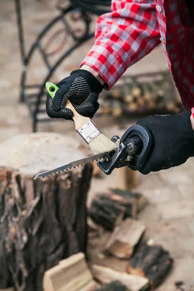 Tool cleaning from sawdust. Hands in a red checked shirt and gloves clean the electric power saw with a brush close-u