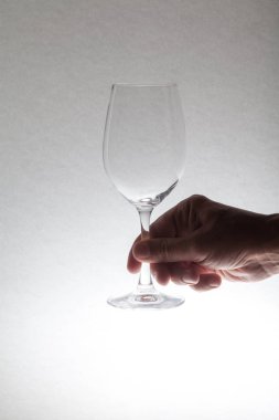 Elini bir boş şeffaf cam şarap kadehi bir gri arka planı kapat-u bir bacak üzerinde tutuyor
