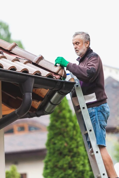 yetişkin adam metal bir merdiven üzerinde duruyor ve bulutlu bir gökyüzü karşı döşenmiş bir çatı onarım