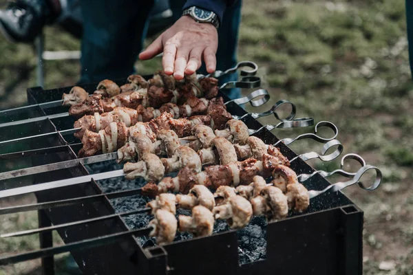 We control the heat in the grill. Hands over skewers with meat and mushrooms. The skewers lie on a metal brazie