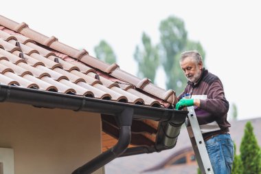 yetişkin adam metal bir merdiven üzerinde duruyor ve bulutlu bir gökyüzü karşı döşenmiş bir çatı onarım