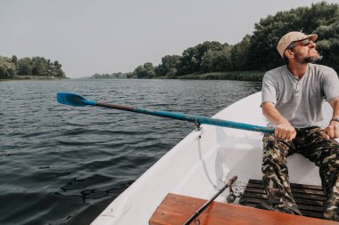 gözlük ve kamuflaj pantolon bir sakallı ortasında bir açık da nehirde kürek tekne kontrol eder.