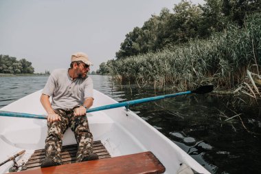gözlük ve kamuflaj pantolon bir sakallı ortasında bir açık da nehirde kürek tekne kontrol eder.