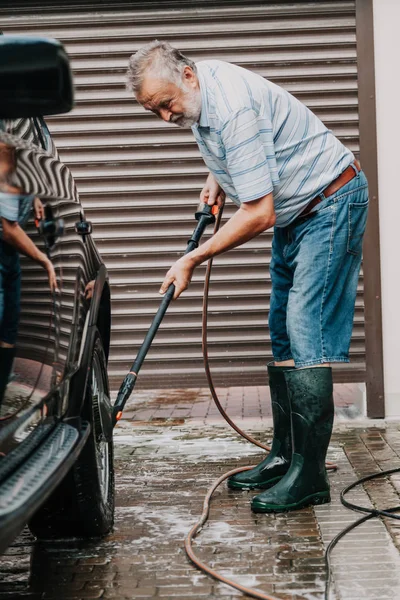 gracious man with a gray beard washes a black car with a special brush on a long handl