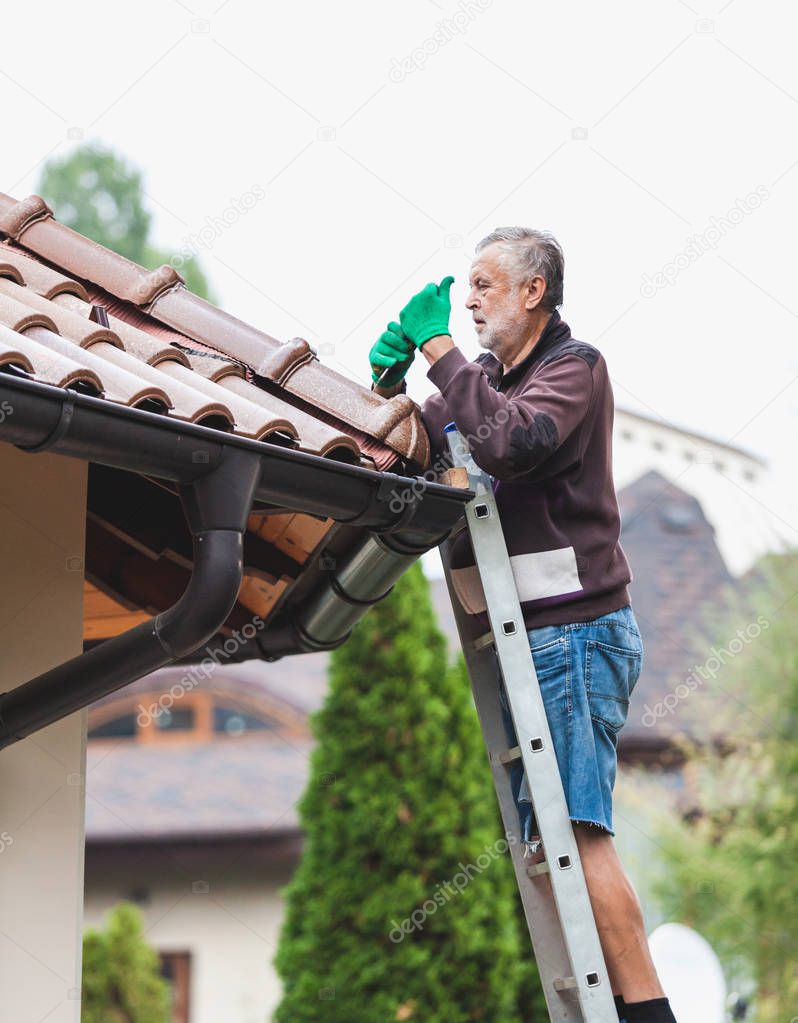 adult man stands on a metal staircase and mounts an element of a tiled roof against a cloudy sk