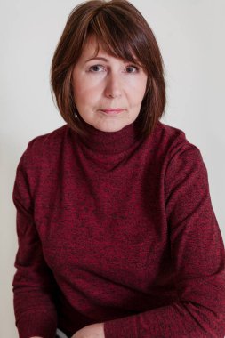 Basit ışık arka plan üzerinde oturan yaşlı kadın portresi. Kadın iyi durumda emeklilik yaşı stil yaşlılıkta gösterir