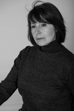 Garip ruh hali. Parlak bir tek sesli arka plan üzerinde oturan Rötuş olmadan bir kadının yakın çekim siyah beyaz portre. Kazaklı düşünceli loo ile yaşlı güzel kadın