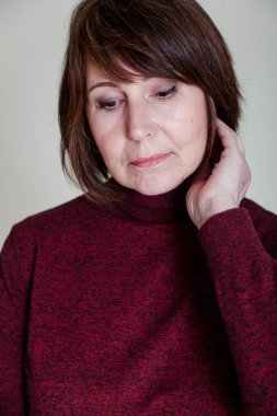 Garip görünüyorsun. Yakın çekim parlak bir tek sesli arka plan üzerinde oturan Rötuş olmadan bir kadın portresi. Düşünceli loo ile Bordo kazaklı yaşlı güzel kadın