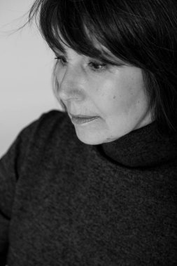 Garip ruh hali. Parlak bir tek sesli arka plan üzerinde oturan Rötuş olmadan bir kadının yakın çekim siyah beyaz portre. Kazaklı düşünceli loo ile yaşlı güzel kadın