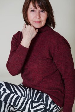 Parlak bir tek sesli arka plan üzerinde oturan Rötuş olmadan bir kadın portresi. Bordo kazaklı fram bakarak gülümseyen yaşlı güzel kadın