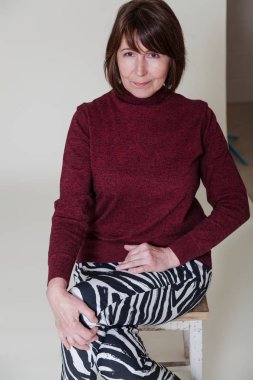 Basit ışık arka plan üzerinde oturan yaşlı kadın portresi. Emeklilik yaşı iyi durumda kadın yaramazca kameraya gülümsüyor ve iyi bir ruh hali ve susuzluk yaşam için yaşlılık gösterir